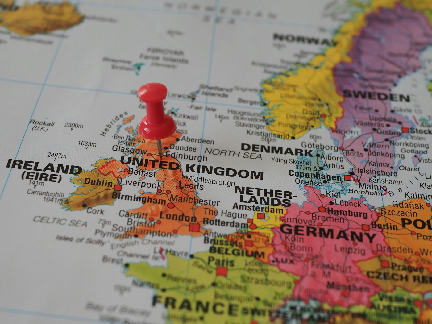 A printed map of north-west Europe with a red push-pin marking the United Kingdom